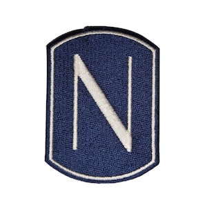 May include: A navy blue embroidered patch with a white letter N in the center. The patch is shaped like a shield with rounded edges.
