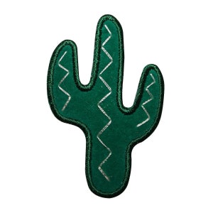 May include: Green felt cactus patch with white zig-zag stitching. The cactus is a popular southwestern motif.
