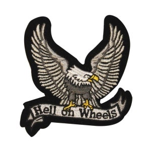 Könnte beinhalten: Schwarzer gestickter Aufnäher mit einem weißen Weißkopfseeadler mit ausgebreiteten Flügeln und einem gelben Schnabel. Der Adler hält ein weißes Banner mit dem Text "Hell on Wheels" in Schwarz.