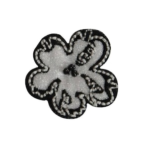 May include: A white flower with black embroidered edges. The flower has a raised, textured surface and is accented with black beads in the center.
