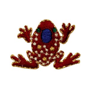 May include: A red frog-shaped embroidered patch with gold trim. The frog has a blue center, green eyes, and white and gold star-like patterns. The patch is designed to be sewn onto clothing or accessories.