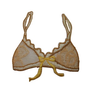 May include: A gold and white embroidered patch in the shape of a bra with a yellow bow.