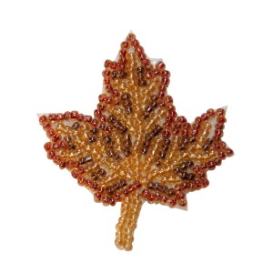 May include: A beaded maple leaf with a brown and orange colour gradient. The leaf is made of small, round beads that are sewn together to create a realistic-looking leaf.