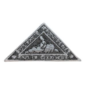 May include: A silver embroidered patch in the shape of a triangle with a black background. The patch features a silver embroidered design of a bear with a tree in the background. The text "Made in Canada" is embroidered around the edge of the patch.