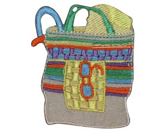 May include: Embroidered patch of a beach bag with a striped design, sunglasses, and a straw hat. The bag is brown with a beige lining.
