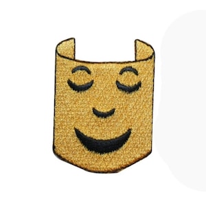Può includere: Un cerotto di feltro giallo con un viso sorridente ricamato. Il viso ha gli occhi chiusi e un ampio sorriso.