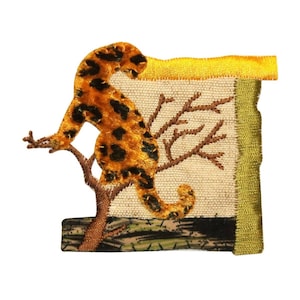 May include: An embroidered patch featuring a brown and orange leopard perched on a tree branch. The patch has a beige background with a green and brown camouflage border.