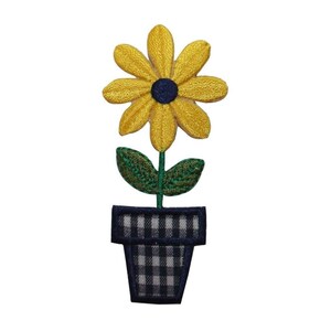 Könnte beinhalten: Eine gelbe Blume mit einem dunkelblauen Zentrum in einem schwarz-weiß karierten Topf. Die Blume hat grüne Blätter.