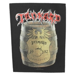 May include: Black patch with a red and silver "Tankard" logo above a brown wooden barrel with a gold eagle and shield. The shield has the text "Tankard 1982 Frankfurt" on it.