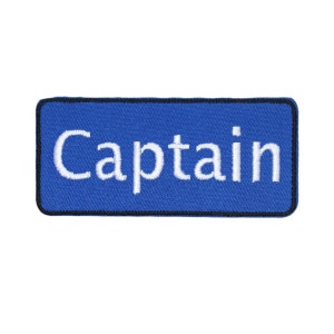 May include: Blue rectangular embroidered patch with white text that reads "Captain".
