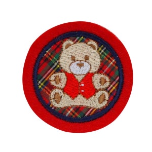 May include: Embroidered patch featuring a teddy bear wearing a red vest, set against a plaid background. The patch has a red border with a navy blue inner ring. The teddy bear is light brown with a detailed embroidered design.