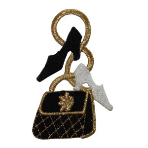 May include: A black handbag with gold trim and a gold chain. Two black high heels and a white shoe are attached to the chain.