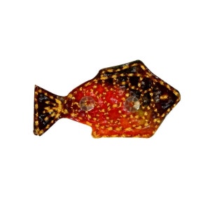 May include: A small, red, black, and gold embroidered fish with two white buttons for eyes.