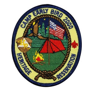 May include: A yellow and blue embroidered patch with the text "Camp Early Bird 2000 Heritage Reservation". The patch features a tent, a campfire, a bird, and an American flag.