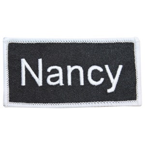May include: White embroidered name tag with the name "Nancy" on a black background.