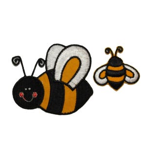 May include: Two embroidered iron-on patches of bees. The larger bee is yellow and black with white wings. The smaller bee is yellow and black with no wings.