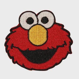 May include: Embroidered patch featuring a smiling red face with large white-rimmed eyes and a yellow nose. The character has a black mouth and is outlined in black. This patch is perfect for adding to clothing or accessories.
