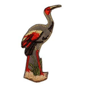 May include: Embroidered iron-on patch of a gray crane with red and black accents standing on a patch of green grass.