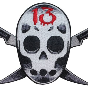 Peut inclure: Masque de crâne blanc avec un numéro rouge "13" qui coule du sang sur le front. Deux couteaux argentés croisés sont derrière le crâne.