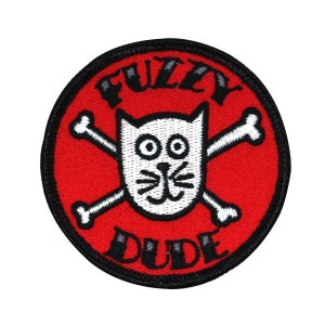 May include: A red and black embroidered patch with a white cat skull and crossbones design. The text "Fuzzy Dude" is embroidered in black on the patch.