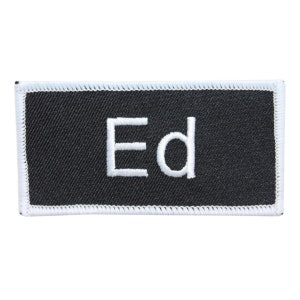 Peut inclure: Écusson en tissu noir avec des coutures blanches autour des bords. L'écusson a le mot "Ed" brodé en blanc.