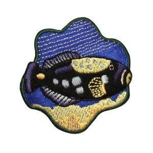 May include: An embroidered iron-on patch depicting a black and white fish with yellow accents swimming in blue water. The fish is surrounded by a yellow and green border.