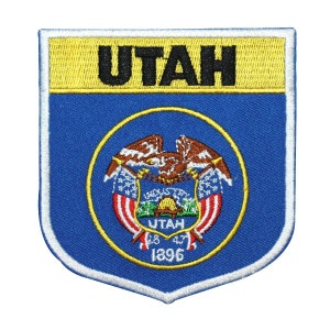 May include: A blue and yellow embroidered patch with the word "UTAH" in black lettering and the state seal of Utah in the center. The seal features a bald eagle with wings spread, a mountain range, and the words "UTAH 1847 1896".
