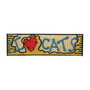 May include: A yellow embroidered patch with the text "I love cats" in blue lettering and a red heart with stitching.