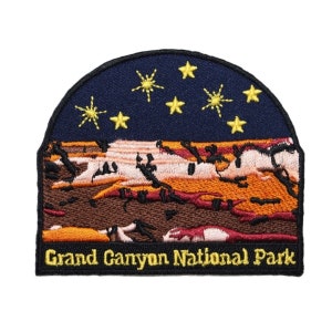 May include: Embroidered patch featuring a nighttime scene of the Grand Canyon National Park with a dark blue sky, orange and brown canyon walls, and yellow stars. The text "Grand Canyon National Park" is embroidered in yellow on a black background.