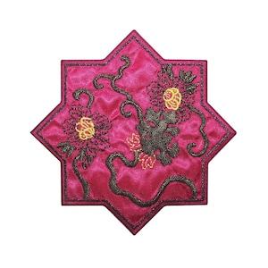May include: A pink, star-shaped coaster with black and yellow embroidered floral designs.