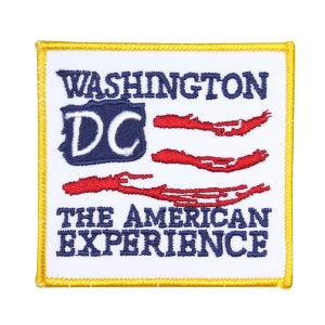 May include: A white embroidered patch with a yellow border. The patch features a stylized American flag with the text "WASHINGTON DC" and "THE AMERICAN EXPERIENCE" below the flag.