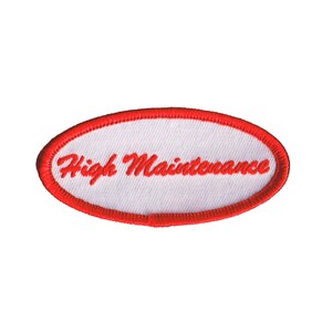 May include: White oval patch with a red embroidered border. The text "High Maintenance" is embroidered in red on the patch.