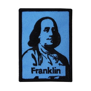 May include: Black and white embroidered patch of Benjamin Franklin's portrait on a light blue background with the word "Franklin" below the portrait.