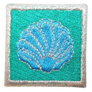 May include: A blue embroidered seashell on a teal green background with a silver border.