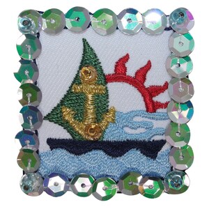 May include: A green sailboat with a gold anchor embroidered on a white background. The sailboat is surrounded by blue waves and a red coral reef. The image is framed with iridescent sequins.