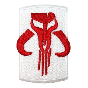 May include: Embroidered patch featuring a red Mandalorian skull symbol on a white rectangular background. The design includes a stylized skull with curved horns and vertical lines, perfect for fans of the Star Wars franchise.