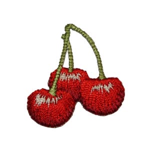 May include: Two red cherries with green stems, embroidered on a white background.