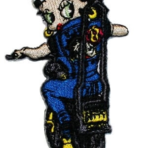 May include: An embroidered patch featuring a cartoon woman with a checkered bandana riding a motorcycle. She is wearing a blue jumpsuit and has a red heart on her chest. The motorcycle is black and has a yellow tire.