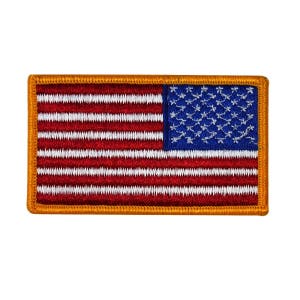 Könnte beinhalten: Gestickter rechteckiger Aufnäher mit der amerikanischen Flagge. Das Design umfasst rote und weiße Streifen, ein blaues Feld mit weißen Sternen und einen goldenen Rand. Geeignet für Kleidung oder Accessoires.