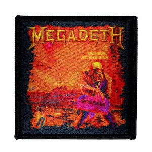 May include: A black and orange embroidered patch with the band name "Megadeth" in yellow lettering. The patch features a figure in a military helmet and a gas mask holding a bag that says "For Sale".