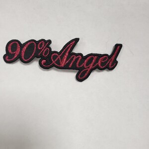 Può includere: Toppa ricamata nera e rossa con il testo "90% Angel" in un carattere corsivo.