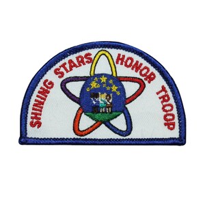 May include: A blue and white half-circle patch with the text "Shining Stars Honor Troop" in red and white lettering. A colorful atom symbol with a blue circle in the center is in the middle of the patch.