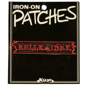 May include: Iron-on patch featuring the words "Hellraiser" in red lettering on a black background. The patch is packaged on a black card with the words "Iron-On Patches" in white lettering.
