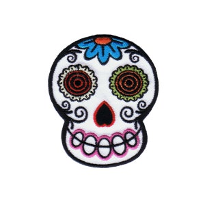 May include: White sugar skull with colorful floral details, including a blue flower on the top, red and green eyes, and pink teeth.
