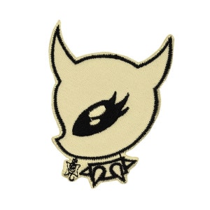 May include: A black and white embroidered patch of a cartoon character with horns, a single eye, and a spiked collar. The character is outlined in black and has a cream-colored face.