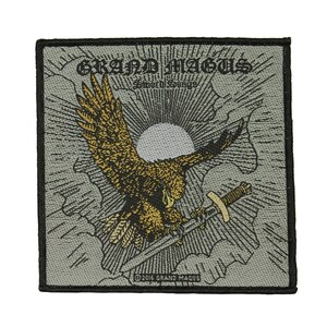 May include: A black and white embroidered patch with a gray background. The patch features a golden eagle with a sword in its talons, flying through the clouds. The text "GRAND MAGUS" and "Sword Songs" is embroidered in black. The text "© 2016 GRAND MAGUS" is embroidered in black at the bottom of the patch.