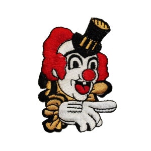 May include: A red and white embroidered clown with a black top hat, a big smile, and a red nose. The clown is pointing with one hand and has a gold and yellow collar.