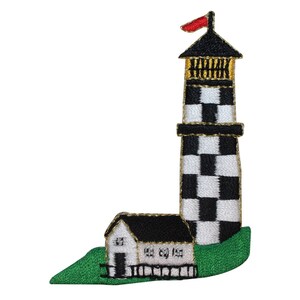 May include: Black and white checkered lighthouse with a red flag on top and a small white building with a black roof at the base. The lighthouse is on a green grassy hill.