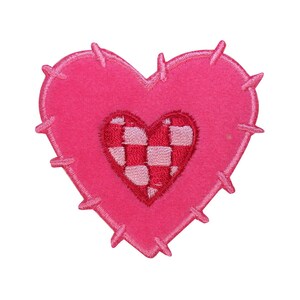 Può includere: Un cuore di feltro rosa con un cuore più piccolo a scacchi rossi e bianchi al centro. I bordi del cuore più grande sono irregolari e hanno un aspetto cucito.