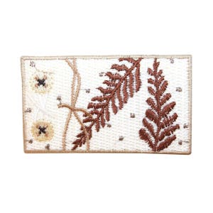 May include: A white embroidered patch with brown fern leaves and white flowers. The patch has a beige border.